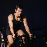 Mies ajaa kuntopyörällä kuntosalilla jalkojen lihaksia ja sydänkuntoa kohoten, mitä lihaksia pyöräily kehittää.