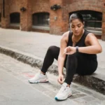 Mustaan ​​trikooon pukeutunut nainen istuu jalkakäytävän reunalla ja miettii seuraavaa siirtoaan urheilukello vertailu -keskustelussa.