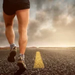 Nainen juoksee tiellä jalat ristissä esitellen juoksemisen kehittämiä lihaksia, kuten mitä lihaksia juoksu kehittää.